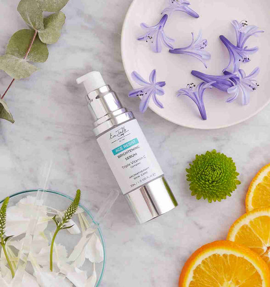 Skincare serum bottle on a marble surface with flowers and oranges