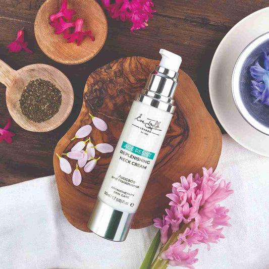 Skincare cream bottle labeled 'Age Resist' on a wooden board with flowers and tea.