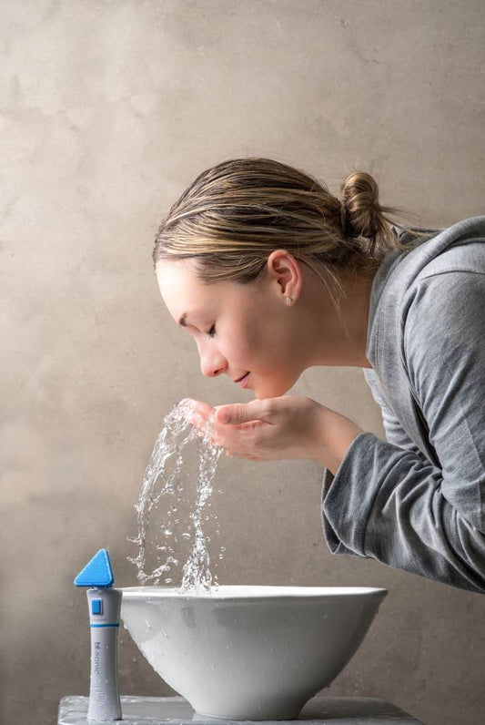 Woman washing face with bt-sonic device in the foreground
