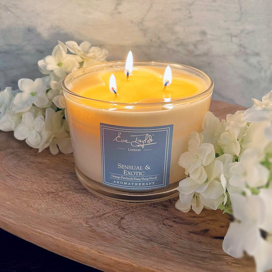 Lit scented 3-wick candle in clear jar with amber wax, branded label