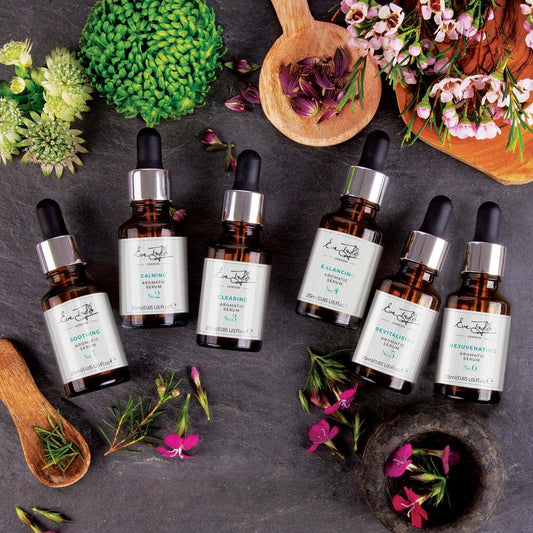 Set of skincare serum bottles with labels on a dark surface with flowers and herbs.