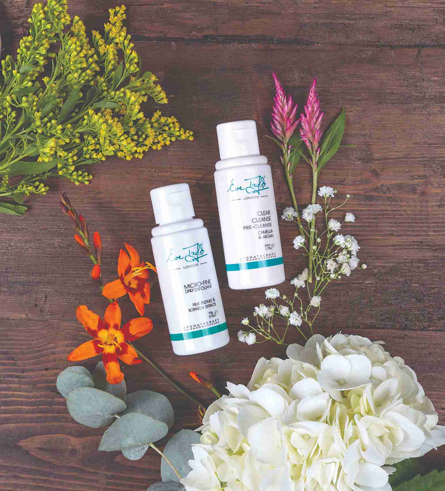 Two skincare bottles on a wooden surface with flowers around them