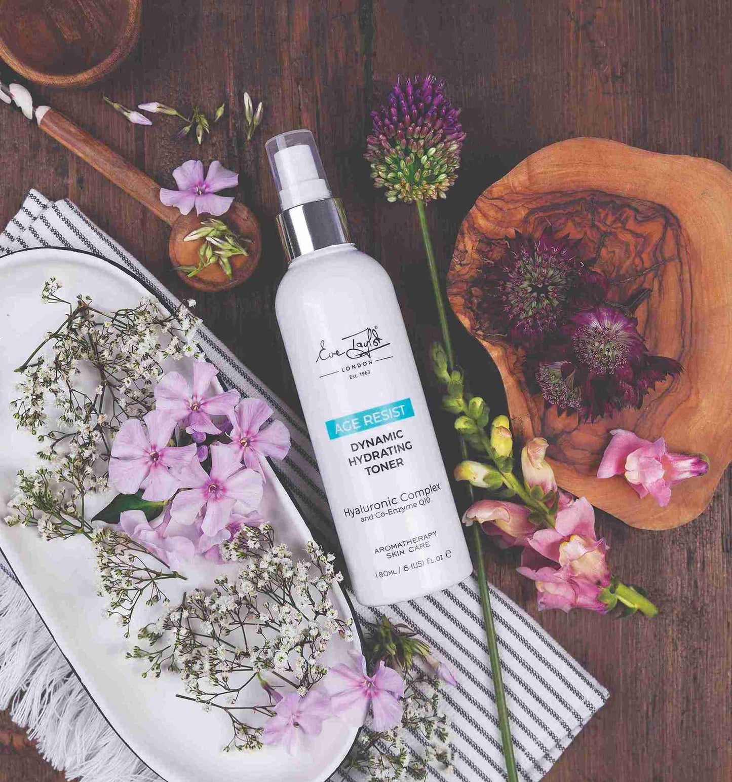 White bottle of dynamic hydrating toner with flowers and wooden elements on a wooden surface