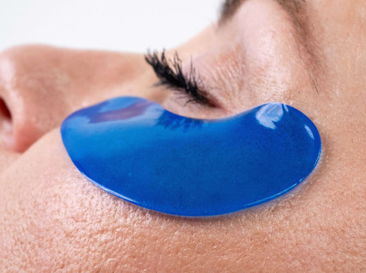 Blue under-eye masque patch, curved gel shape resting on skin near eyelashes