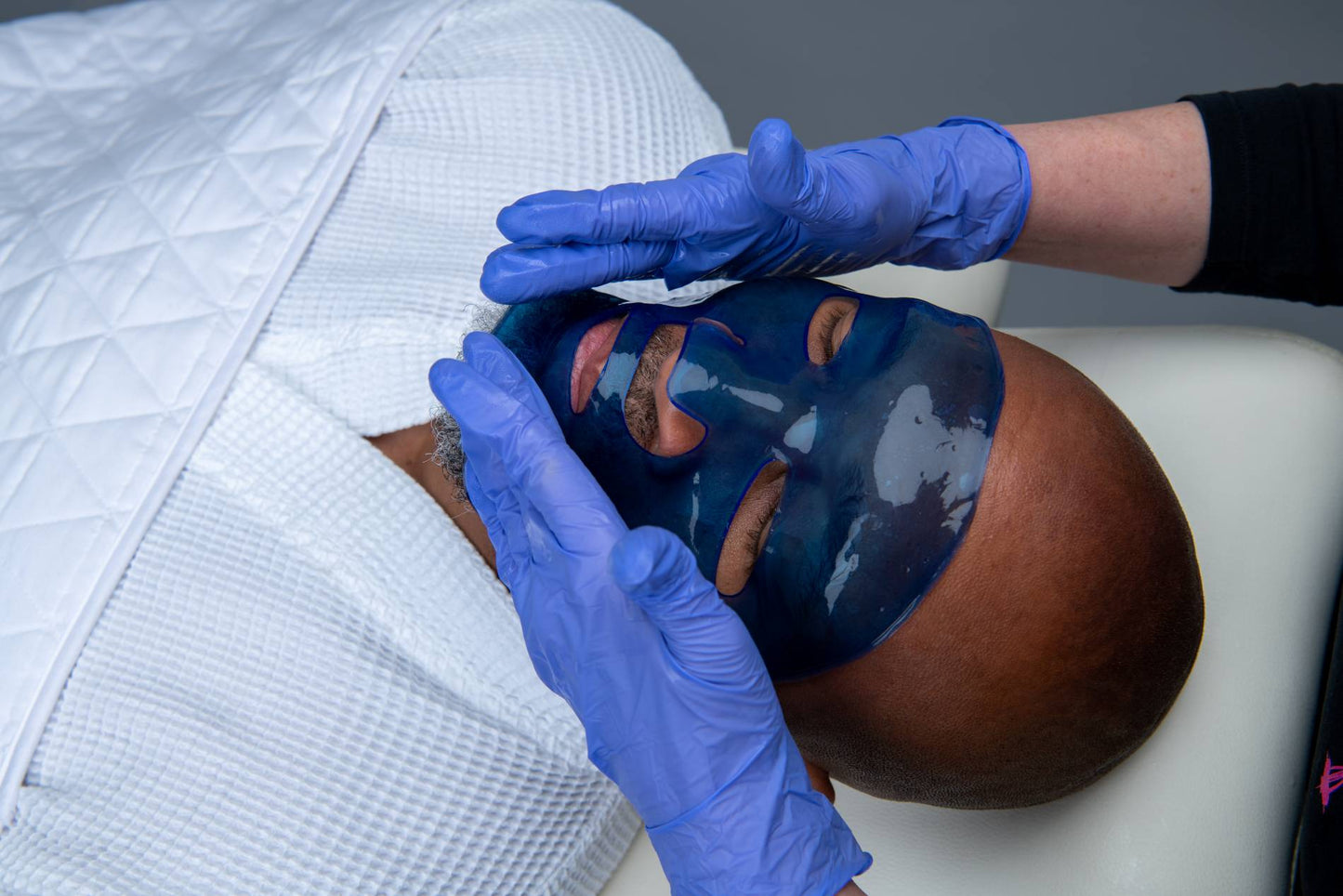 Blue face masque being adjusted on a person’s face with blue gloves