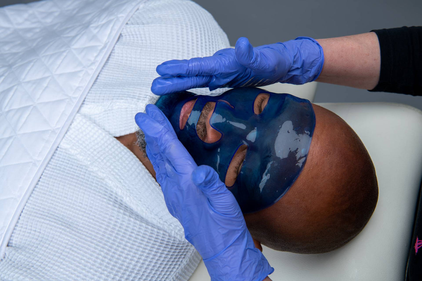 Blue hyaluronic face masque being smoothed by gloved hands