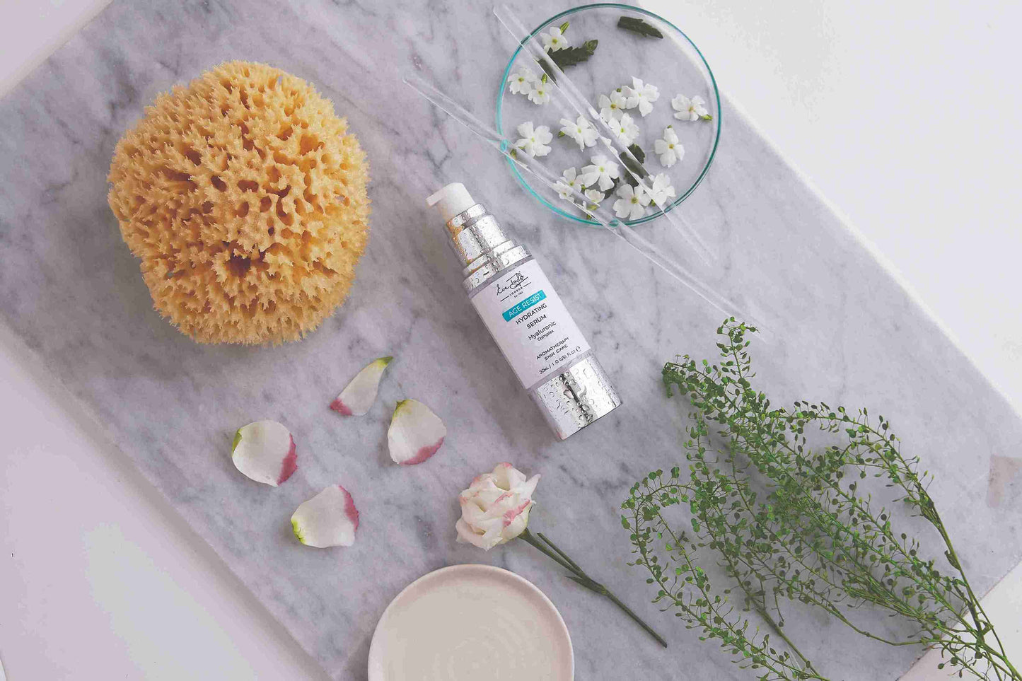 Skincare product with a sponge, flowers, and greenery on a marble surface